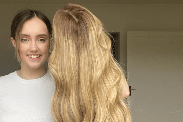 Woman Holding A Long, Wavy Hair Wig With A Smile On Her Face